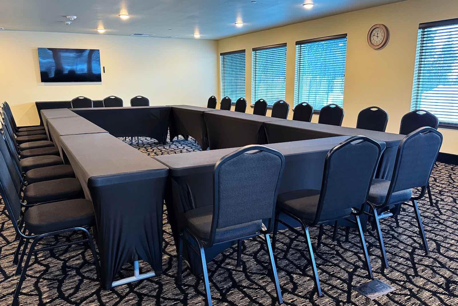 Homer, Alaska meeting room. Tables arranged in a big rectangle with brown table cloths, chairs and a TV on the wall.